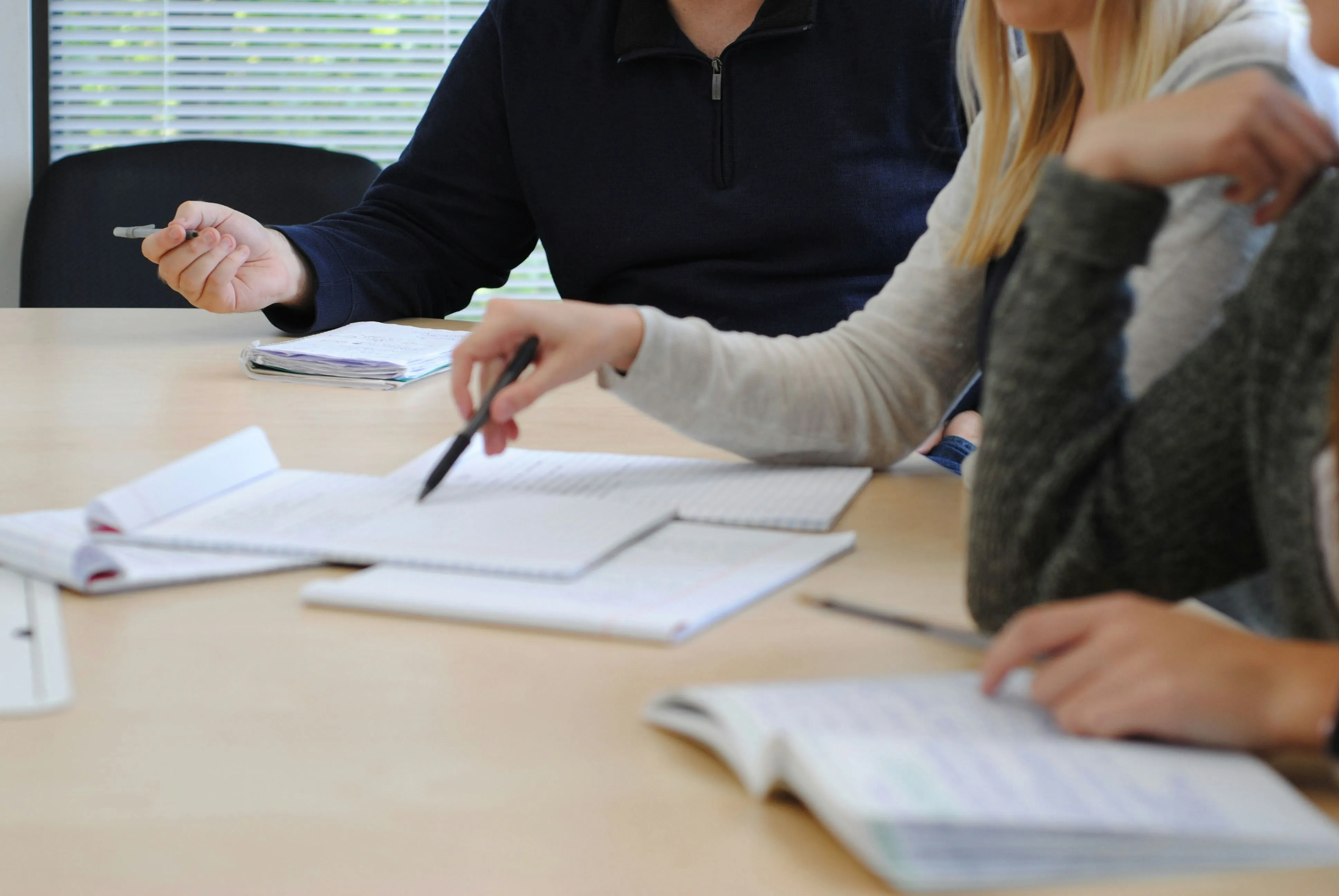 Deux personnes étudient ensemble des documents étalés sur une table claire, stylos en main